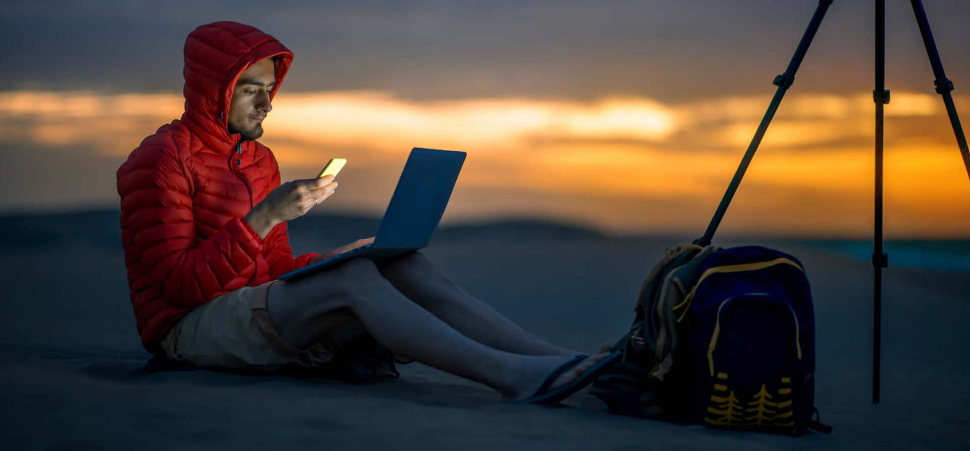 Man on mobile device with laptop and dslr